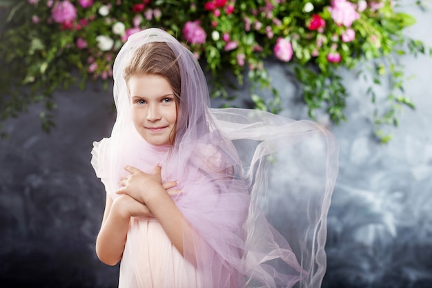 Hermosa niña jugando con tela ligera contra las flores. Retrato de la niña bonita.