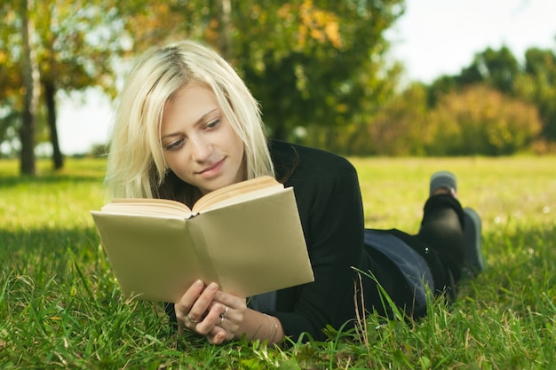 Hermosa niña leyendo un libro en el parque sobre el césped