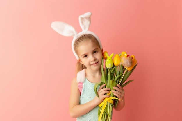 Hermosa niña linda con orejas de conejo de Pascua sonriendo y sosteniendo un ramo primaveral de tulipanes amarillos