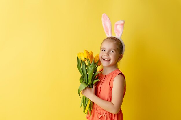 Hermosa niña linda con orejas de conejo de Pascua sonriendo y sosteniendo un ramo primaveral de tulipanes
