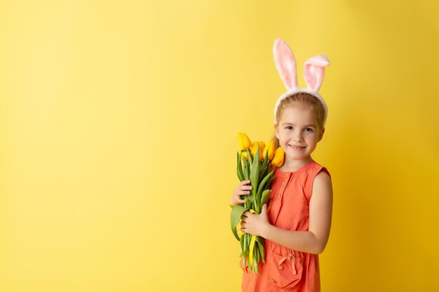 Hermosa niña linda con orejas de conejo de Pascua sonriendo y sosteniendo un ramo primaveral de tulipanes