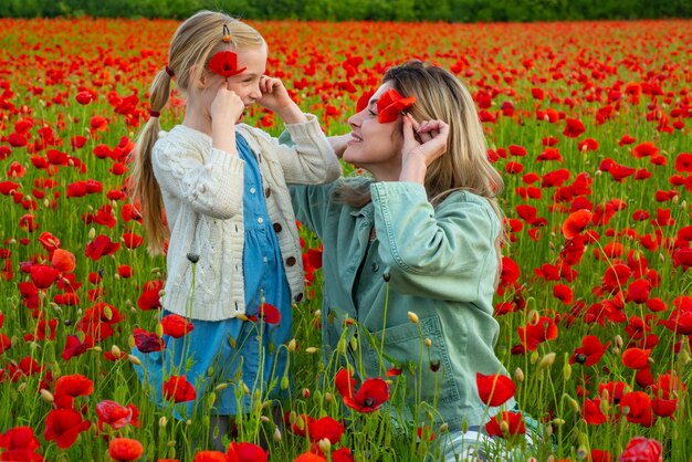 Hermosa niña con madre joven lleva ropa informal en el campo de la familia de flores de amapola o