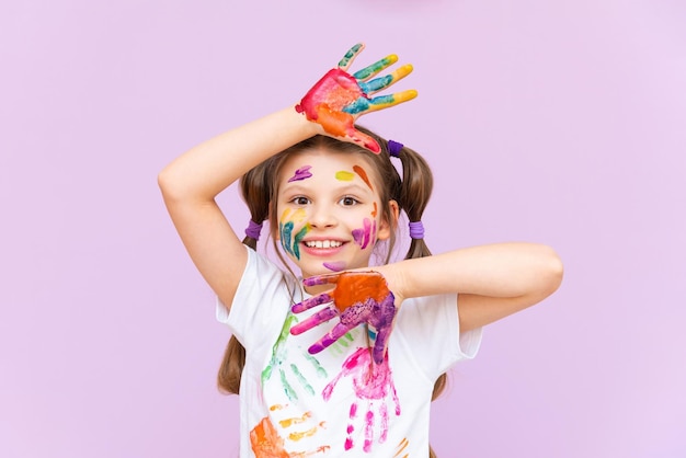 Una hermosa niña manchada con pinturas multicolores en un fondo rosa aislado se divierte sonriendo