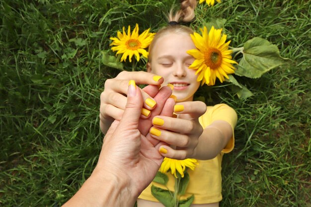 Una hermosa niña con una manicura amarilla se encuentra en la hierba con girasoles