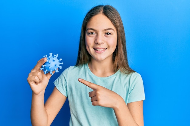 Hermosa niña morena sosteniendo un juguete de virus sonriendo feliz señalando con la mano y el dedo