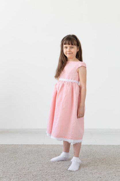 Hermosa niña morena con un vestido rosa posando en una pared blanca. El concepto de niños lindos. Espacio publicitario