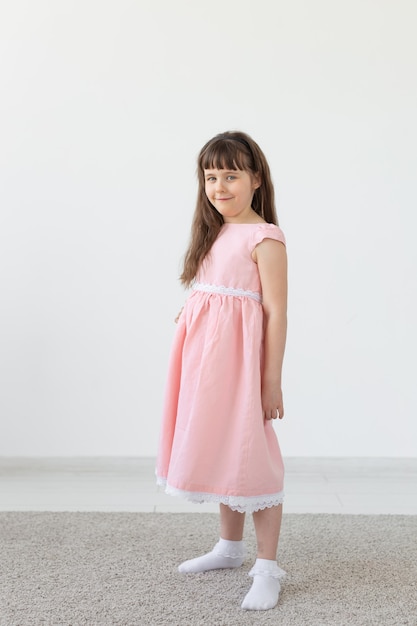 Hermosa niña morena con un vestido rosa posando sobre una superficie blanca