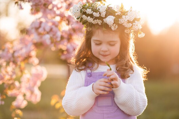 Hermosa niña niño lindo usar corona de flores sobre puesta de sol y cerezo floreciente