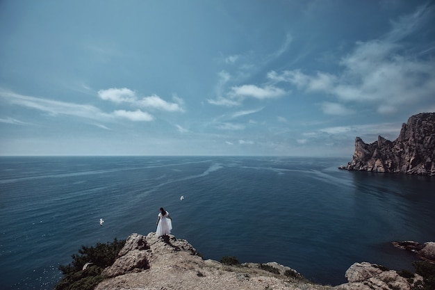 Una hermosa niña, una novia, con un vestido blanco, está de espaldas sobre una roca