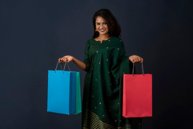 Hermosa niña o mujer india sosteniendo y posando con bolsas de compras en un fondo oscuro