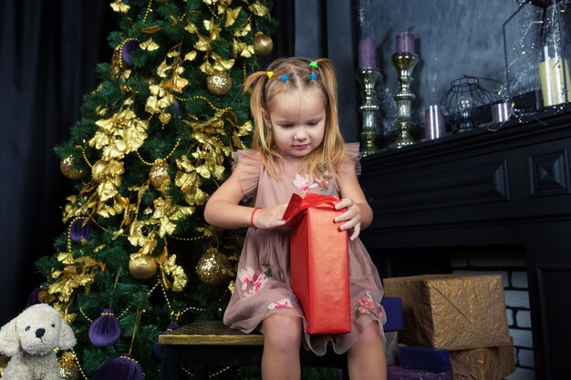 Hermosa niña con ojos azules abre regalo de Santa Claus cerca del árbol de Navidad