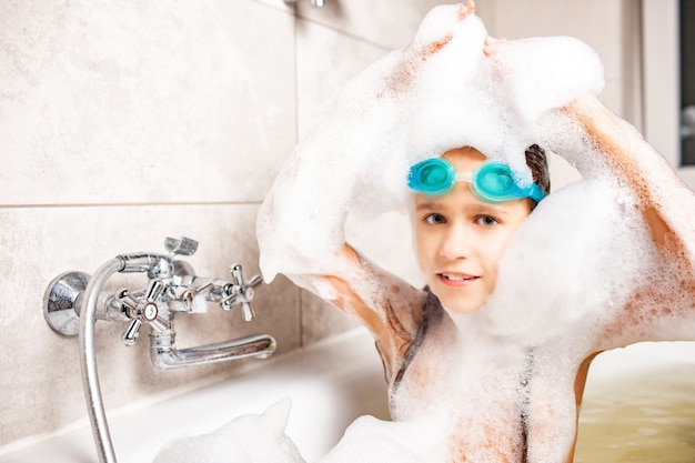 Hermosa niña de ojos azules en gafas de natación se baña en un baño de espuma