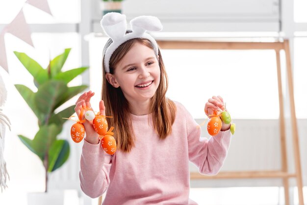 Hermosa niña con orejas de conejo sosteniendo huevos pintados en sus manos y sonriendo en Pascua