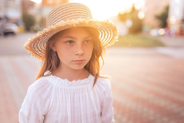 Hermosa niña con pecas en la cara Chica en una blusa blanca y con un sombrero de paja en la cabeza puesta de sol