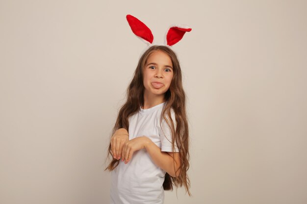 una hermosa niña con el pelo largo en una camiseta blanca con orejas de conejo sonríe Pascua