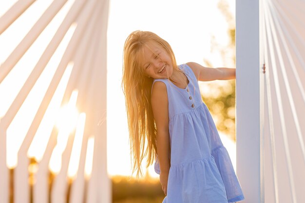 hermosa niña con el pelo largo y rubio camina al atardecer en el parque de la ciudad en verano