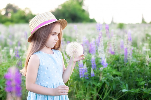 Hermosa niña de pie en un campo de flores en la hierba verde y sostiene un diente de León. Disfruta la naturaleza. Saludable niña sonriente en el césped de verano. Alergia sin concepto. Infancia. Copia espacio