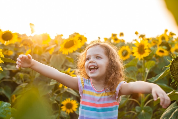 Hermosa niña de pie en los girasoles y levantando las manos