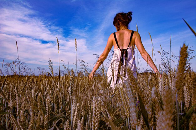 Una hermosa niña posa en un campo de trigo contra un cielo azul.