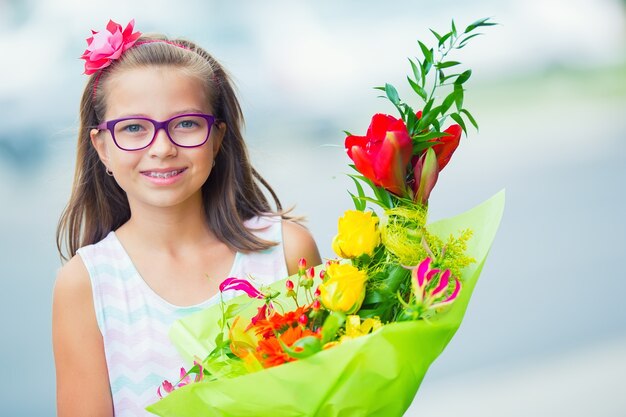 Hermosa niña posando con un gran ramo de flores. Chica con frenillos y gafas.