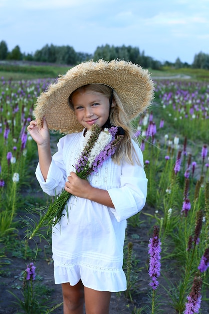 Hermosa niña en un prado con un ramo de flores