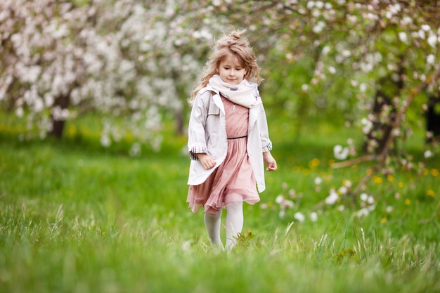 Hermosa niña preadolescente con cabello largo y rubio disfruta de la floración de la manzana de primavera. Niña preescolar corriendo en flores de árboles de jardín. Primavera. Copia espacio