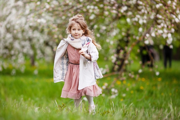 Hermosa niña preadolescente con cabello largo y rubio disfruta de la floración de la manzana de primavera. Niña preescolar corriendo en flores de árboles de jardín. Primavera. Copia espacio