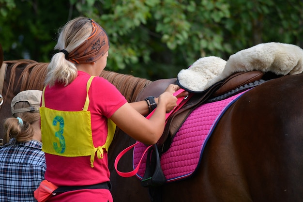 Una hermosa niña prepara a su caballo para la competencia.