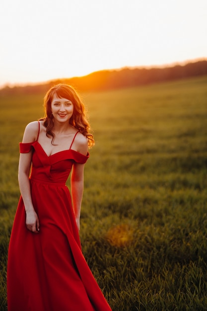 Una hermosa niña en primavera con un vestido rojo está caminando en un campo al atardecer