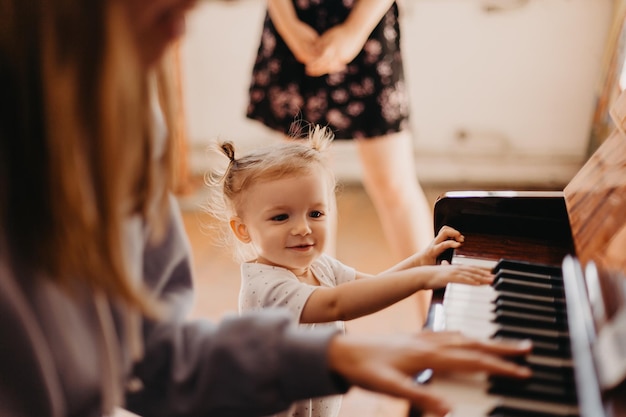 Hermosa niña con rabo en la cabeza carismática cantando la canción al piano que toca mamá