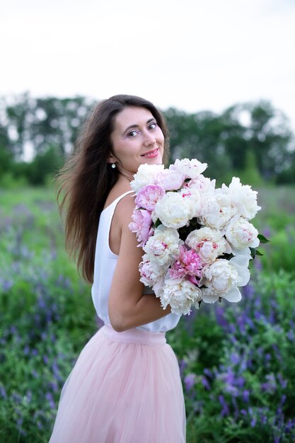 Hermosa niña con ramo de flores de color rosa peonías en un campo