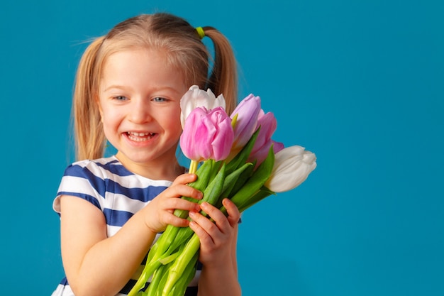 Hermosa niña con ramo de tulipanes contra la pared azul