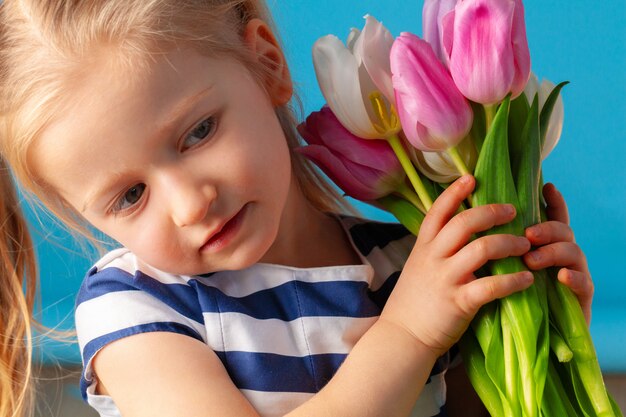 Hermosa niña con ramo de tulipanes sobre fondo azul