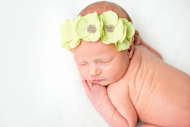 Hermosa niña recién nacida en corona floral durmiendo en una manta blanca