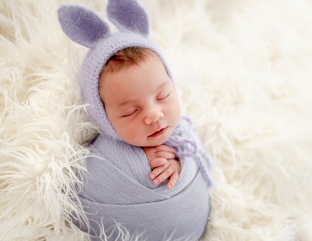 Hermosa niña recién nacida envuelta en tela y con sombrero con orejas de conejo durmiendo en la piel durante la sesión de fotos de estudio. Niño lindo niño durmiendo la siesta