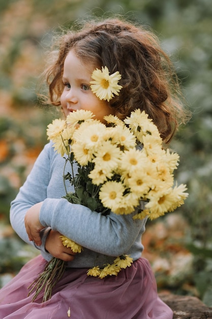 hermosa niña rizada con camisa azul en el parque con flores en otoño tarjeta de salud de otoño