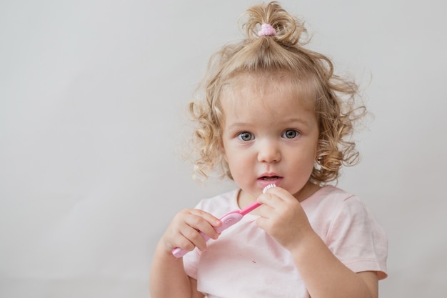 Hermosa niña rizada con cepillo de dientes en la pared gris