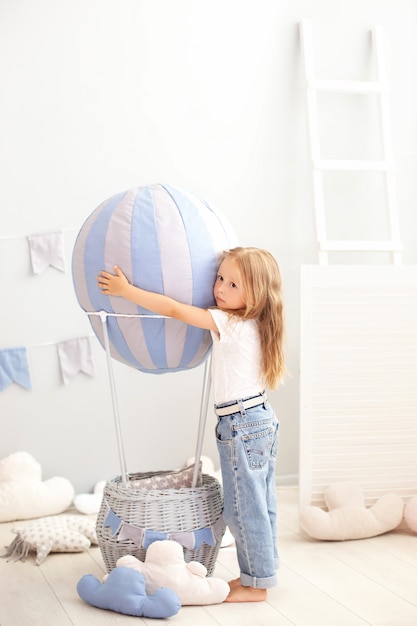 Hermosa niña en ropa casual se encuentra de un globo decorativo. El niño juega en la habitación de los niños.