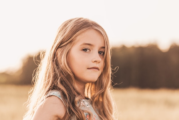 Hermosa niña rubia con cabello largo caminando por un campo de trigo