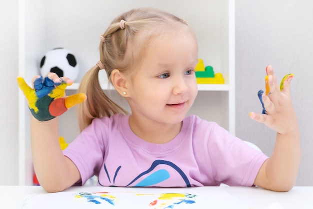 Hermosa niña rubia con coloridos pintados en sus manos, sonriendo felizmente