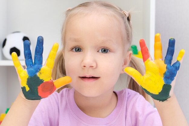 Foto hermosa niña rubia con coloridos pintados en sus manos, sonriendo felizmente