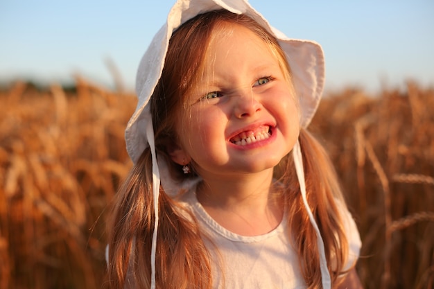 Una hermosa niña rubia se encuentra en un campo de trigo con ropa blanca