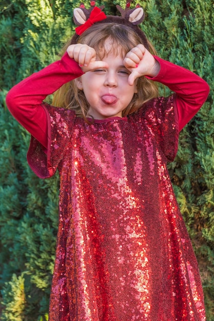 Hermosa niña rubia posando en ropa de Navidad y fondo de pinos