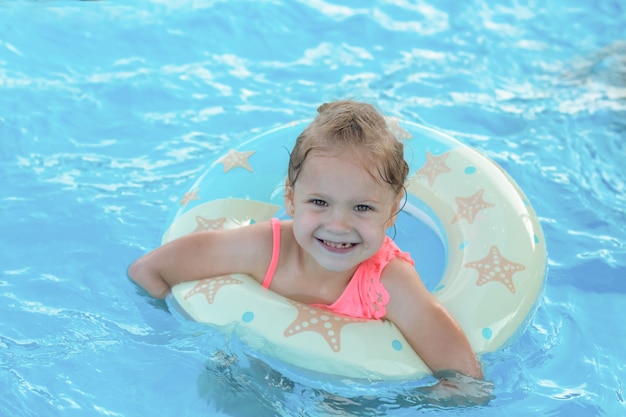 Hermosa niña rubia sonriente feliz nada en la piscina en un salvavidas