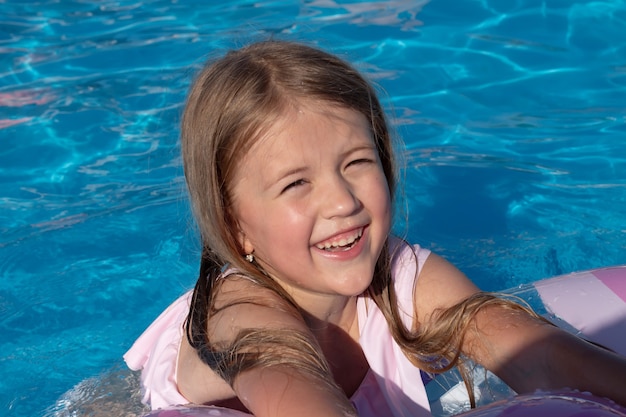 Hermosa niña rubia sonriente feliz en un traje de baño rosa nada en la piscina