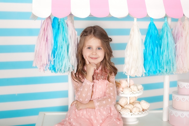 Hermosa niña sentada en la mesa con caramelos. El bar de cumpleaños de Candy. Retrato de un primer plano de cara de bebé.