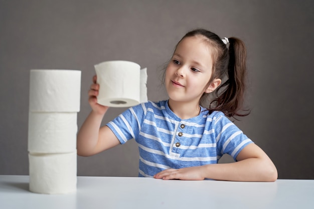 Hermosa niña sentada en la mesa y papel higiénico escaso