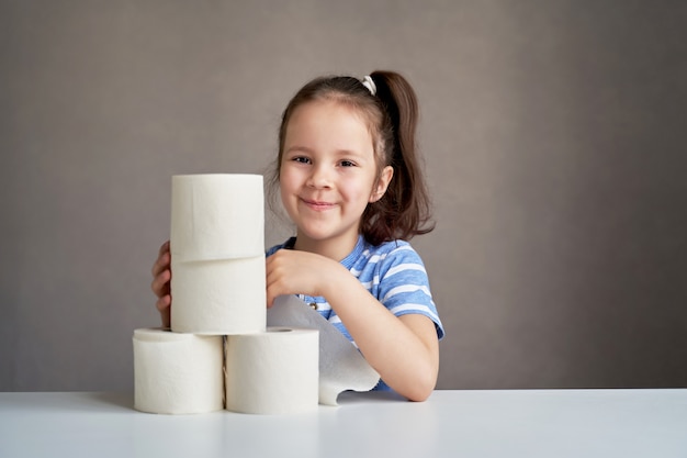 Hermosa niña sentada en la mesa y papel higiénico escaso