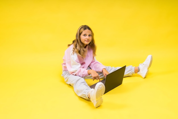 Hermosa niña sentada en un piso claro con una computadora portátil gris y un espacio vacío sonriente