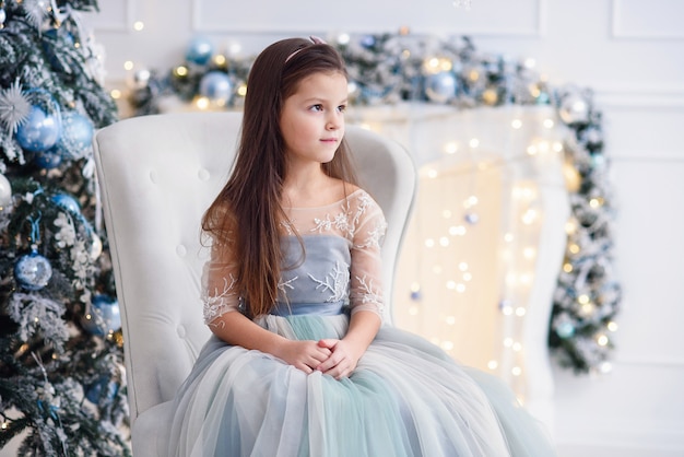 Hermosa niña sentada en la silla en el brillante interior de Navidad decorado.